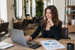 Salon owner reviewing hair salon KPIs on a laptop with charts and calculator